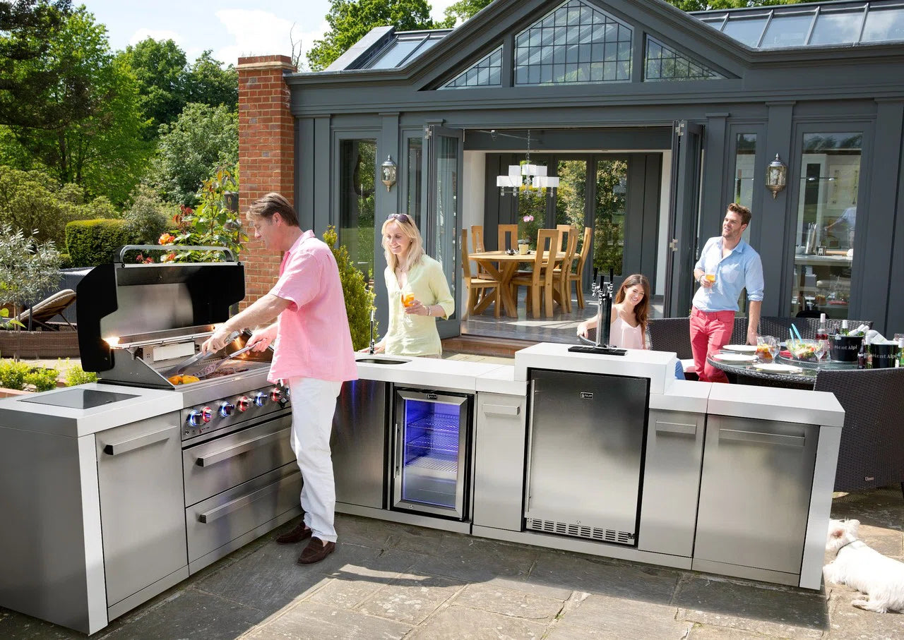 Outdoor kitchen setup with people around a grill and dining area.