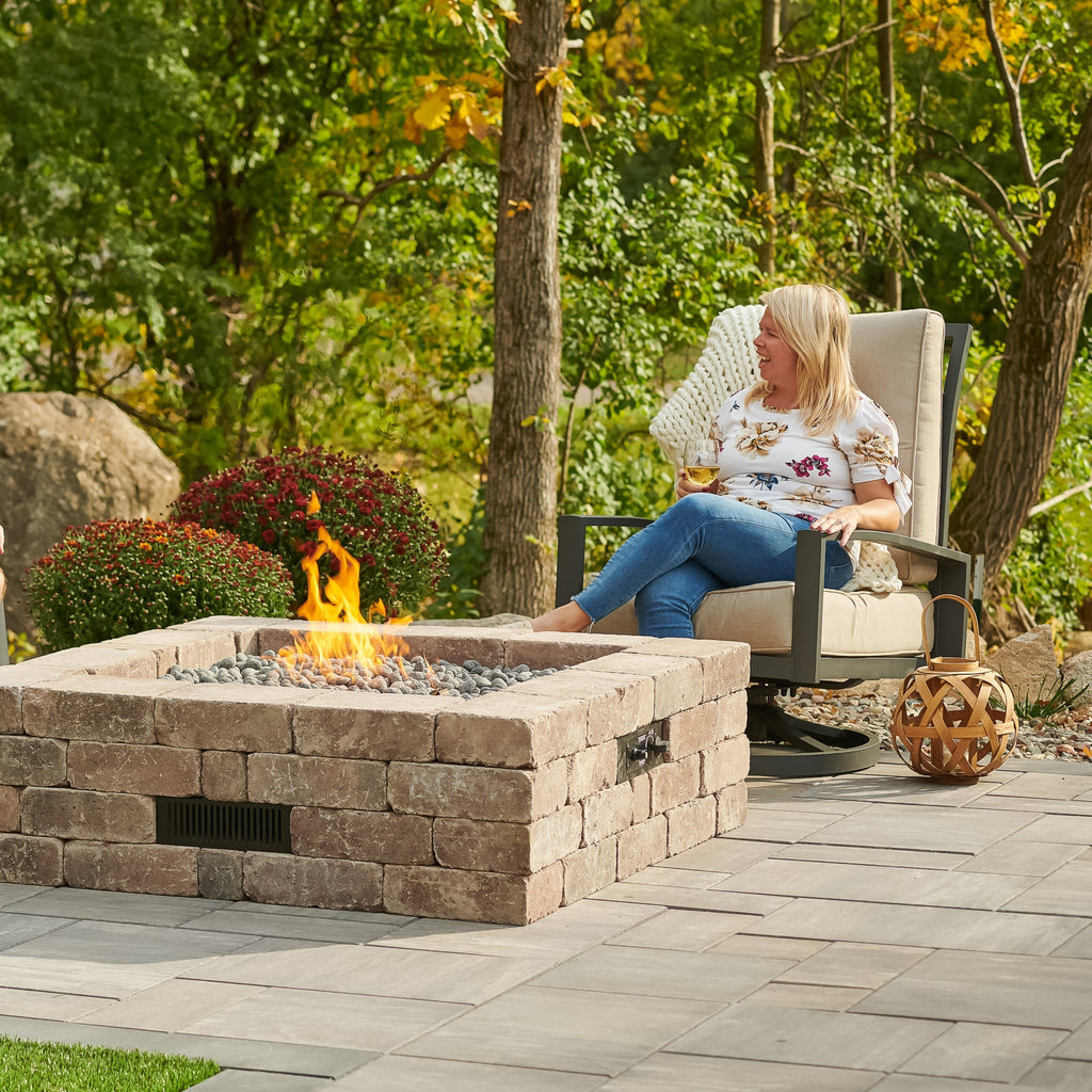 Person relaxing next to the Bronson Block Square Gas Fire Pit Kit on a patio