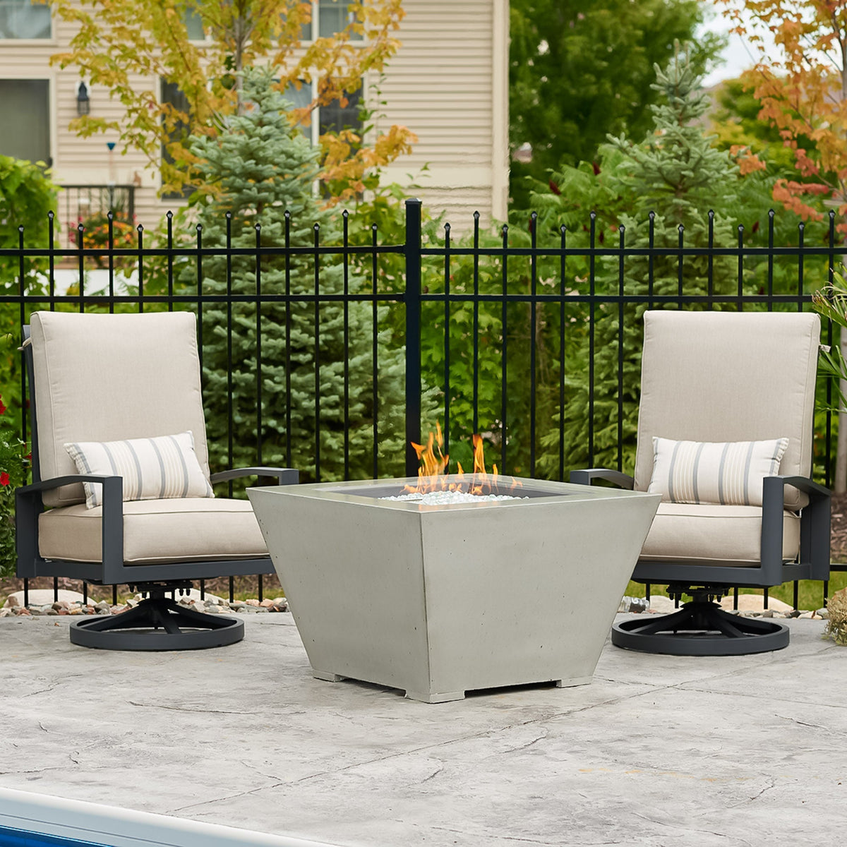 Cove Concrete Trapezoid 37-inch gas fire pit bowl in Natural Grey with lit flame beside patio furniture