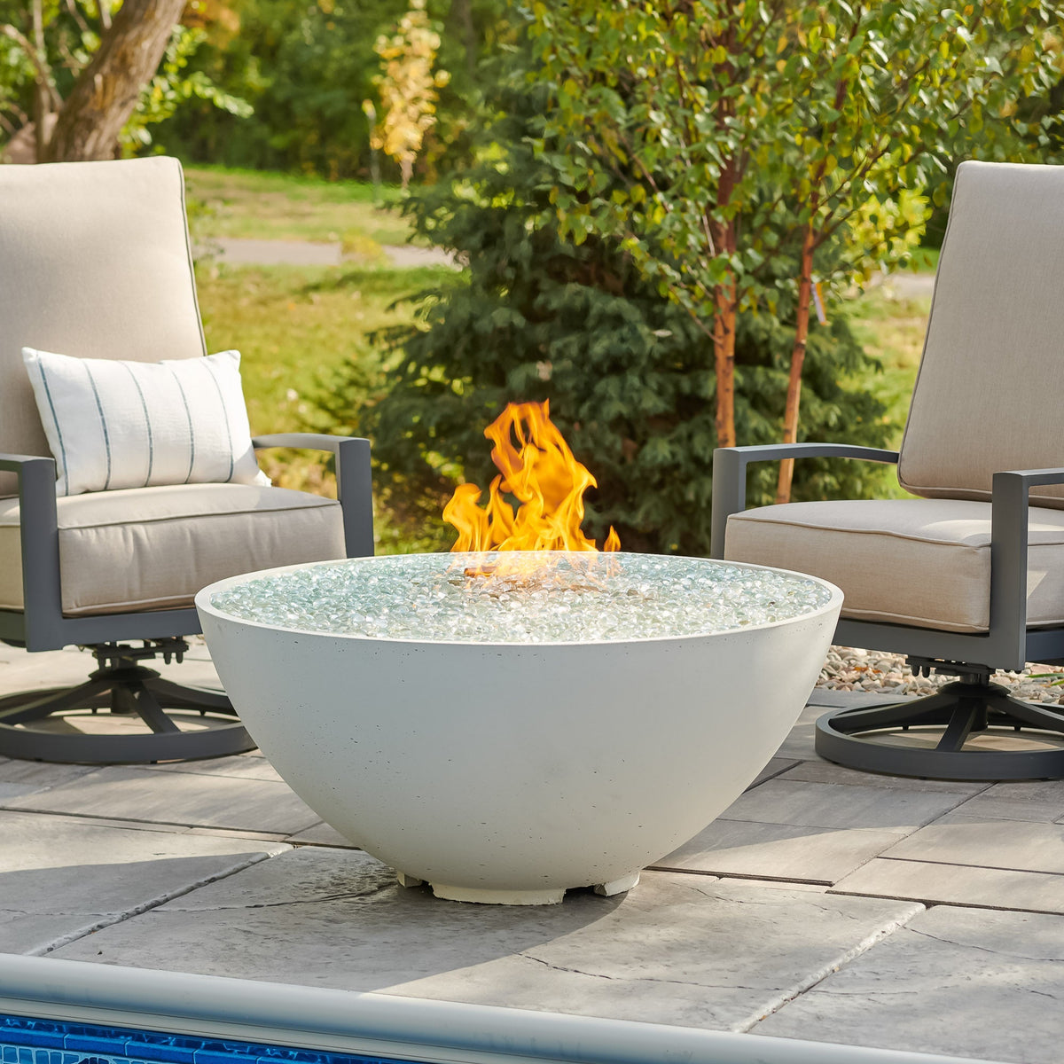 White Cove Concrete Edge 42-inch gas fire pit bowl with a large flame surrounded by lounge chairs